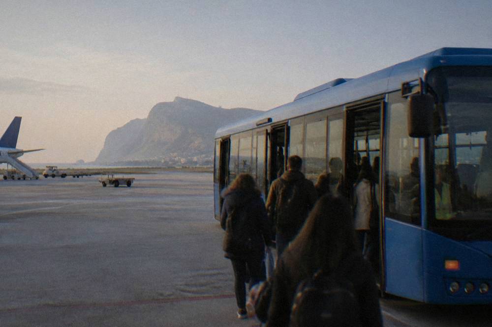 A blue airport bus parked at a Palermo terminal with passengers boarding