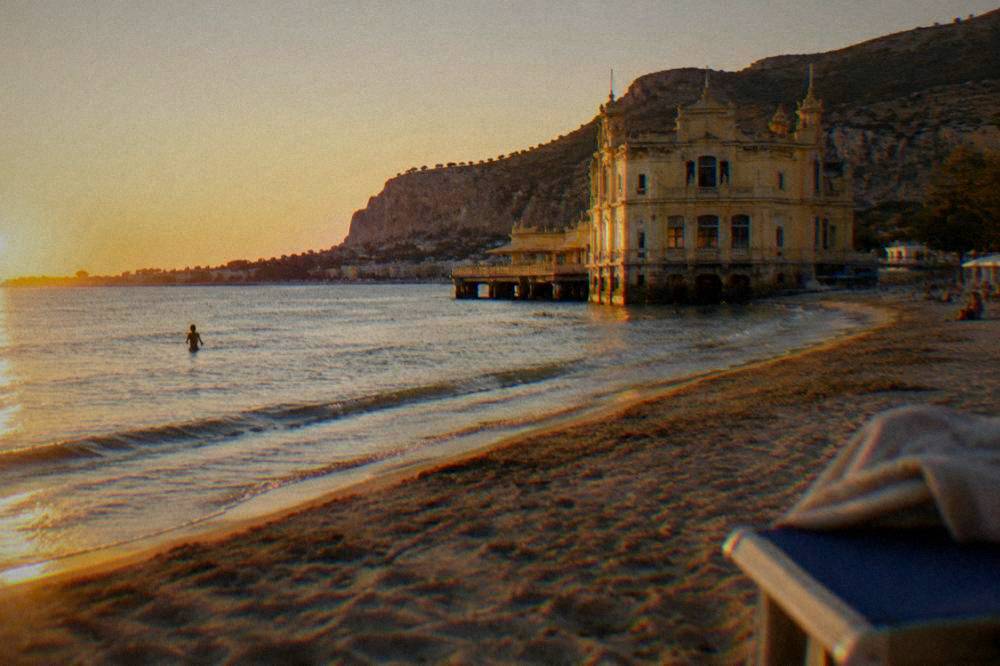 A sandy town beach with a historic stone building close to the water
