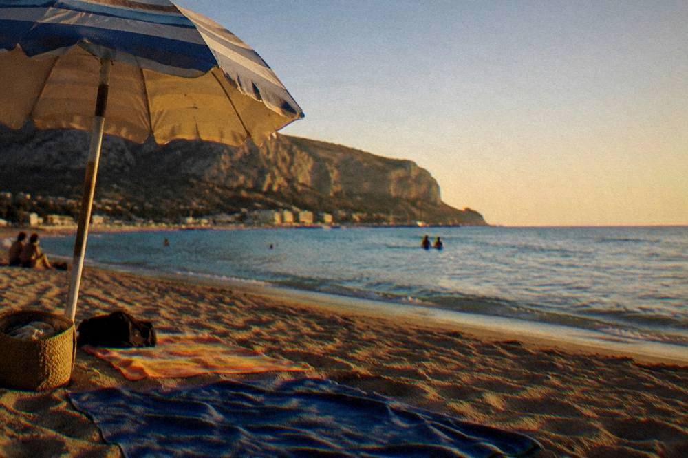 A parasol and towels on open sand with calm sea and clear sky