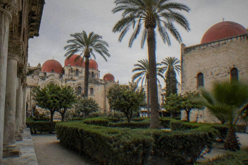 A quiet cloister garden with palm trees and red-domed chapels at San Giovanni degli Eremiti in Palermo