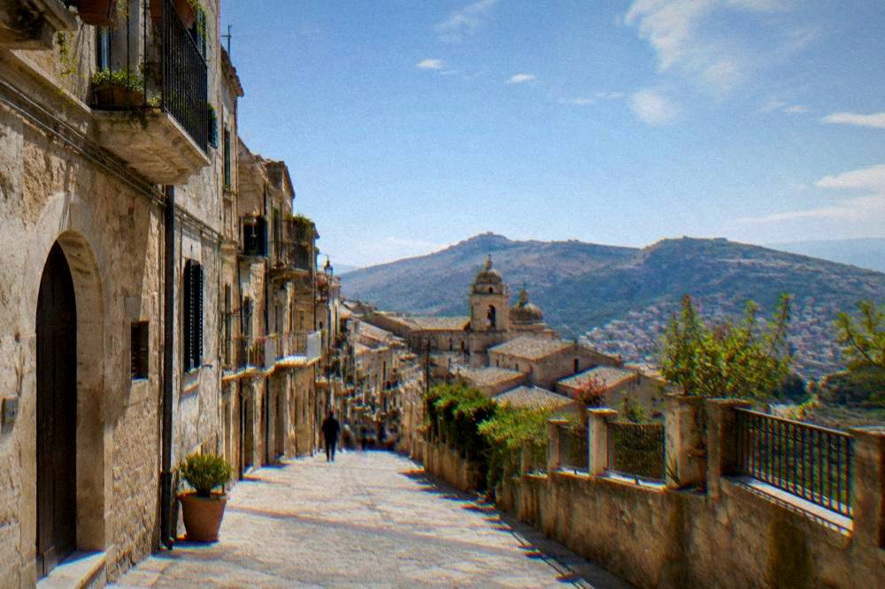 A hill town street in Corleone with stone buildings under a bright sky