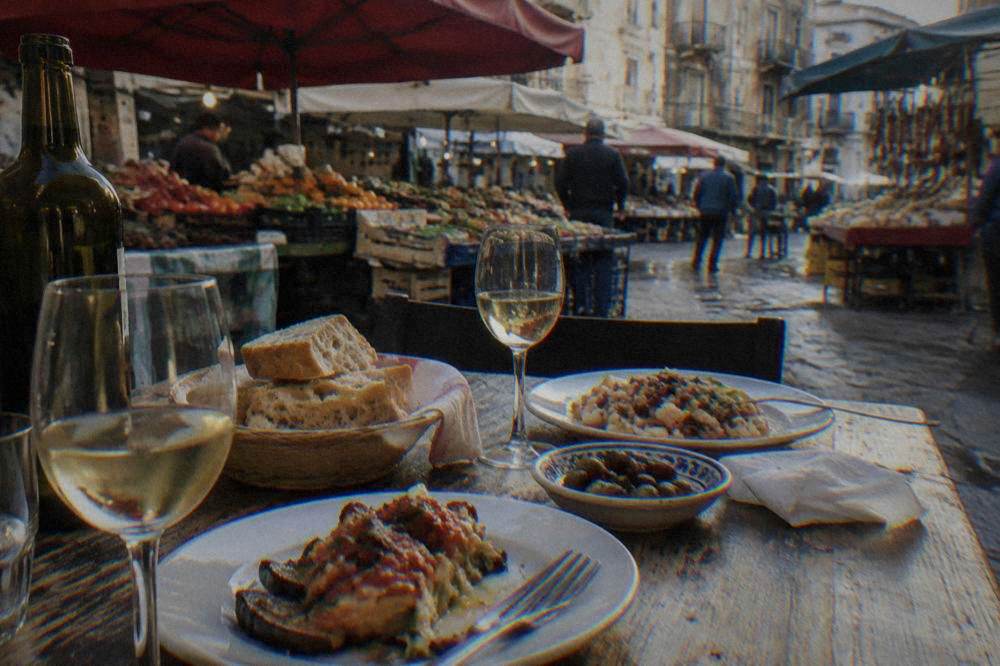 A table set with wine glasses, fresh bread and plates of cooked food for a shared meal