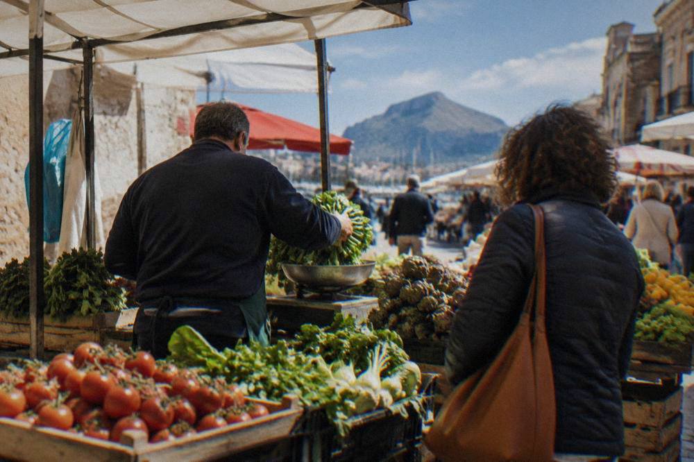 A vendor weighing vegetables at a market stall while a customer watches