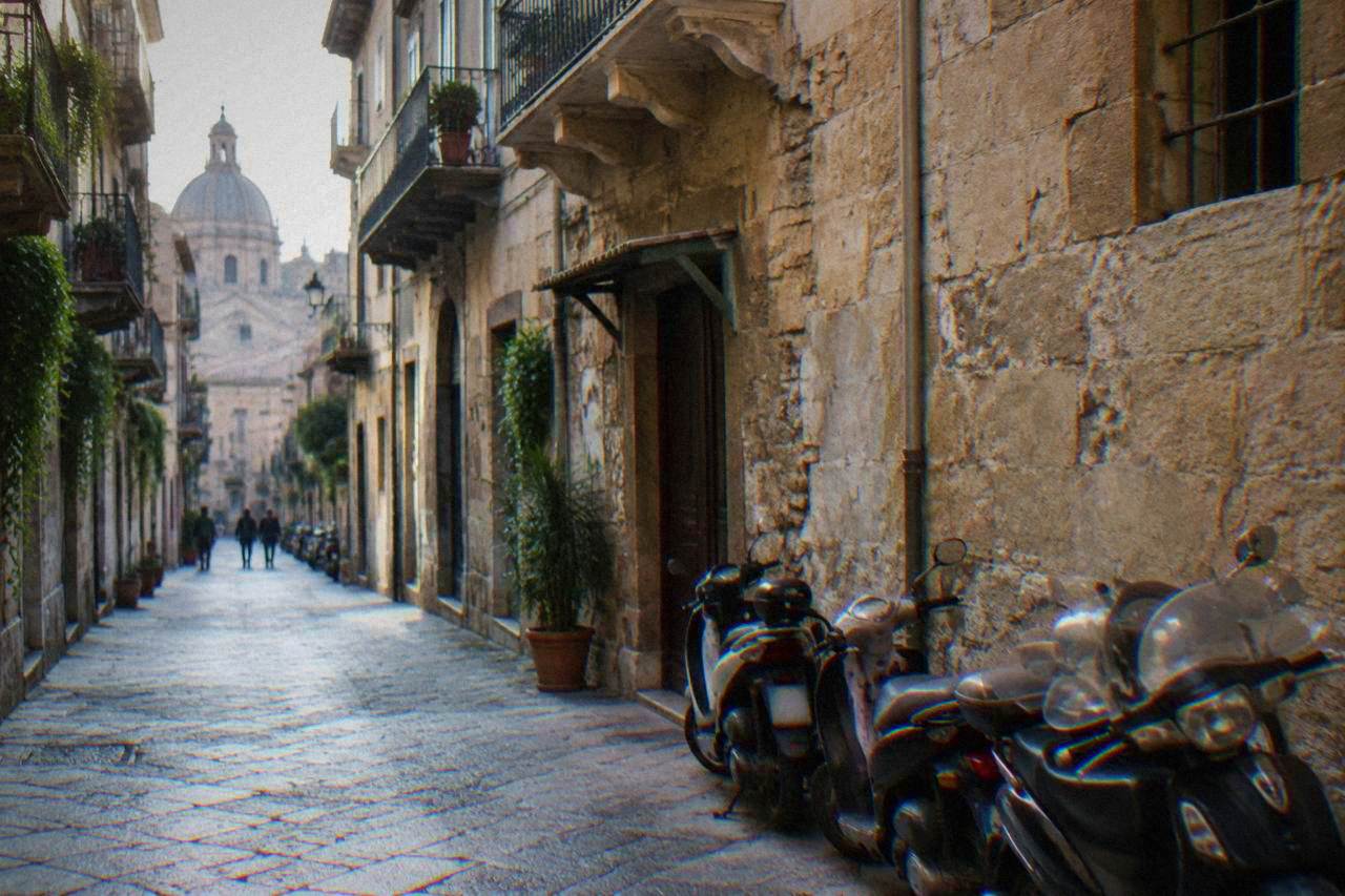 A narrow street in the Palermo old centre with parked scooters along the wall