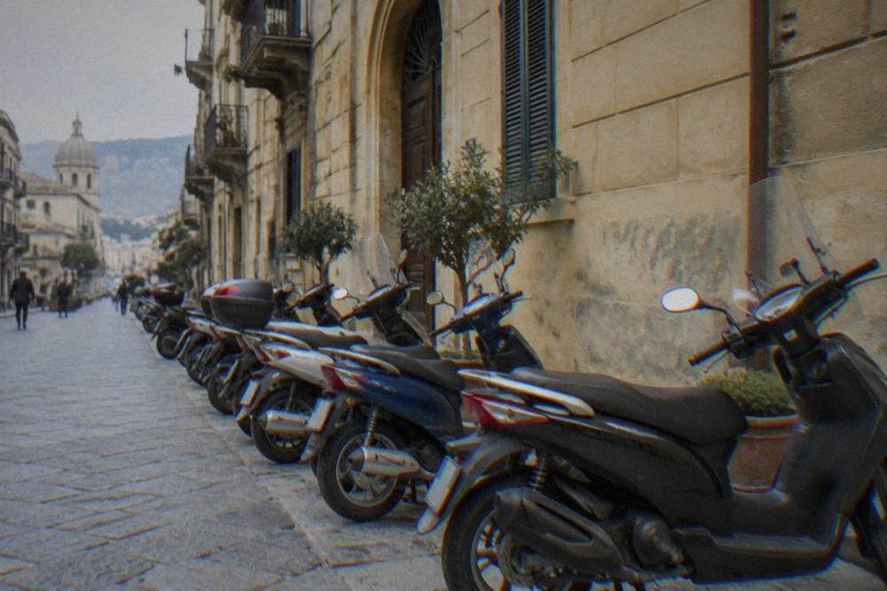 Scooters parked in a row beside a sunlit building in Palermo
