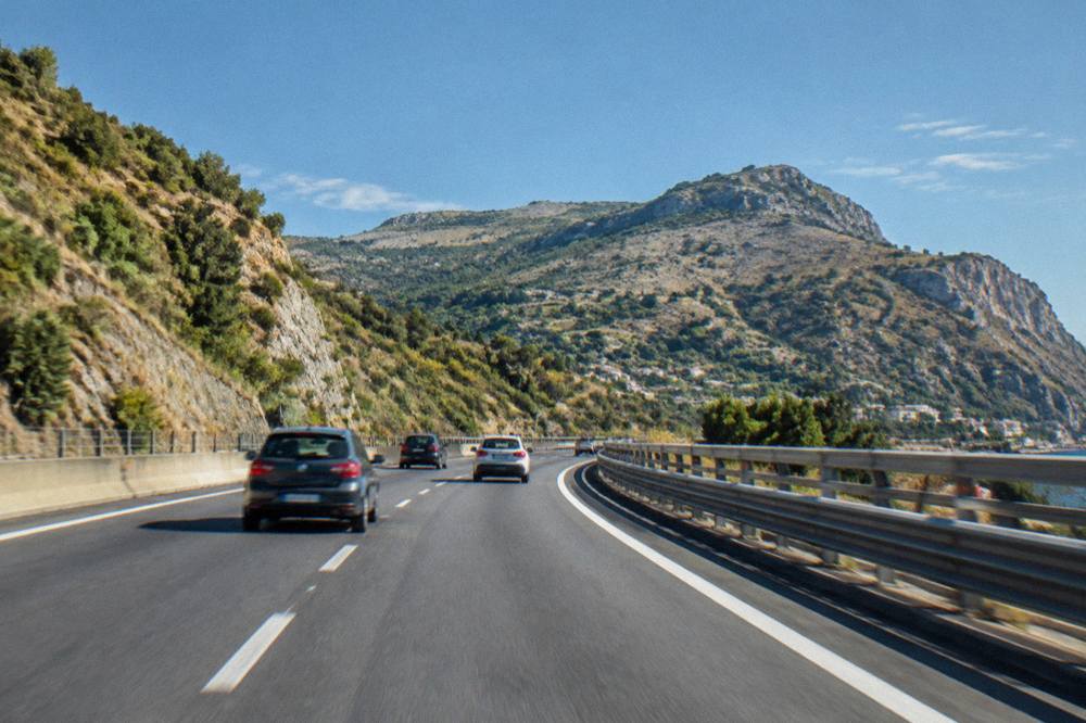A Sicilian motorway curving between hills under a clear sky with cars at speed
