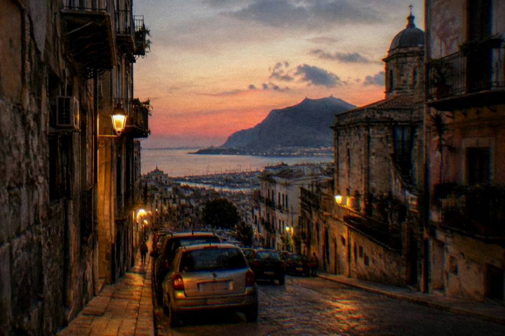 An evening view of a Palermo street with cars parked and warm street lighting