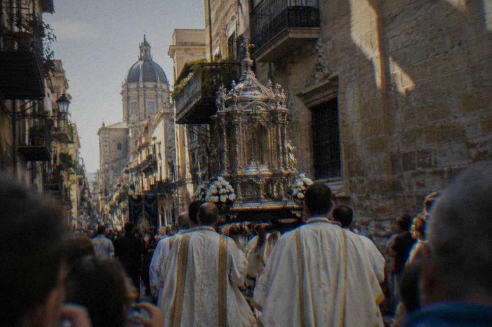 A religious procession with a silver reliquary carried through a narrow Palermo street lined with onlookers