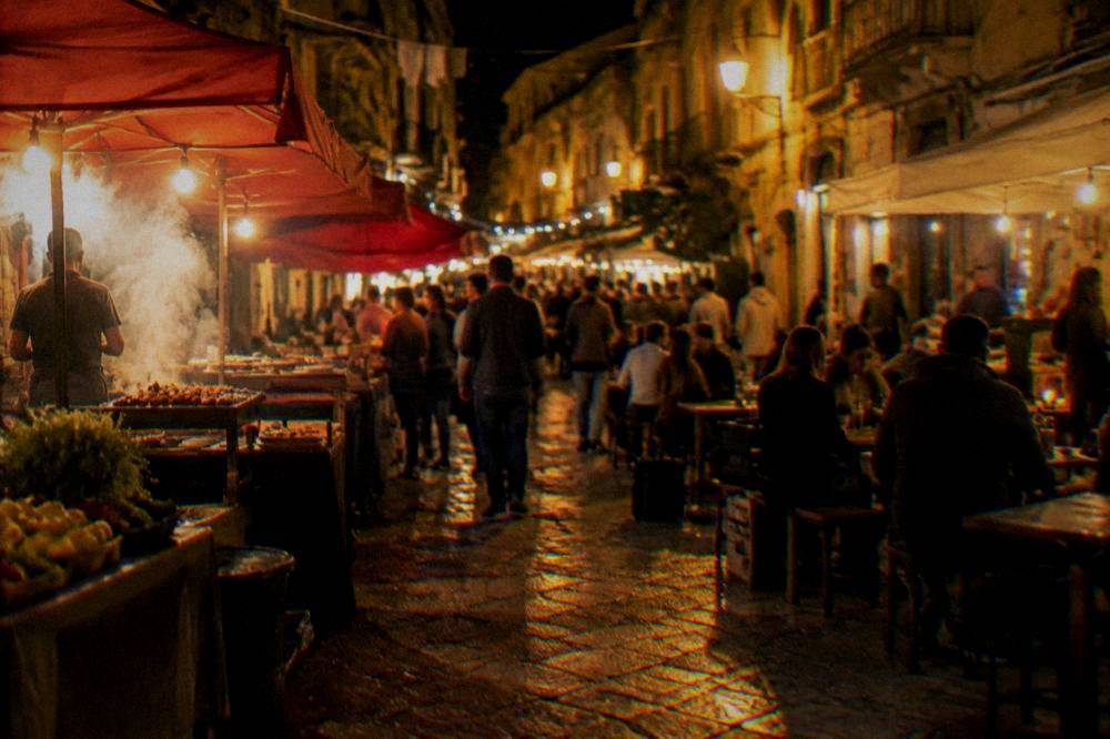 A lit Palermo street at night with people gathered around food stalls and outdoor tables