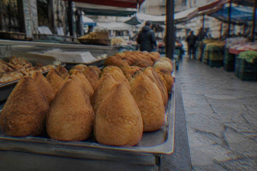 Golden fried arancine arranged in a row at a Palermo market counter