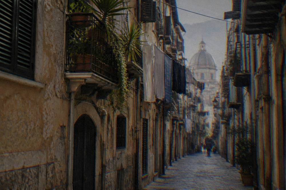A narrow Palermo old-town street with tall shuttered buildings and laundry overhead
