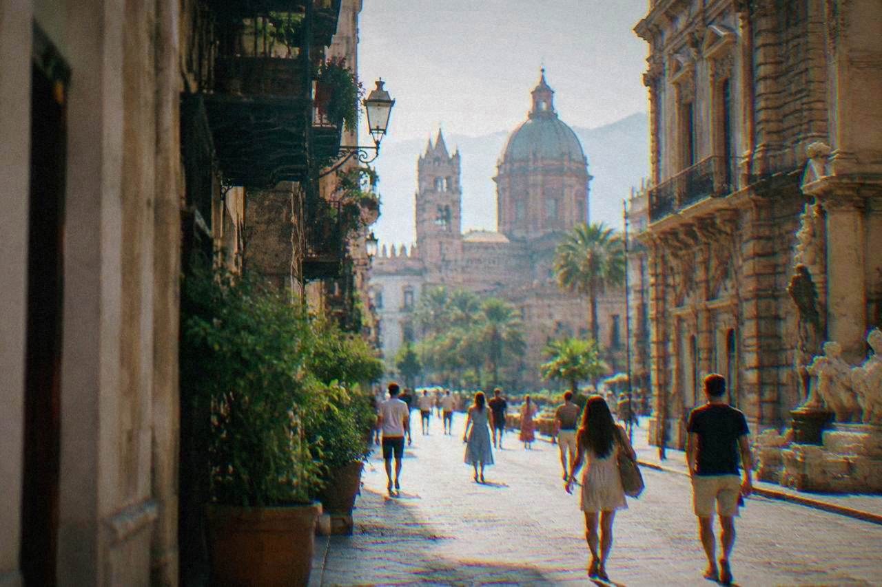 Sunlit historic street in Palermo with ornate buildings and people walking in light summer clothing