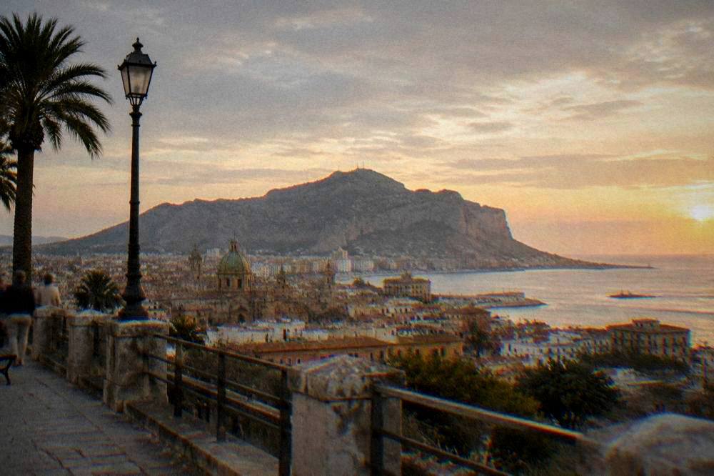 View over Palermo rooftops toward the sea at golden hour with Monte Pellegrino in the distance