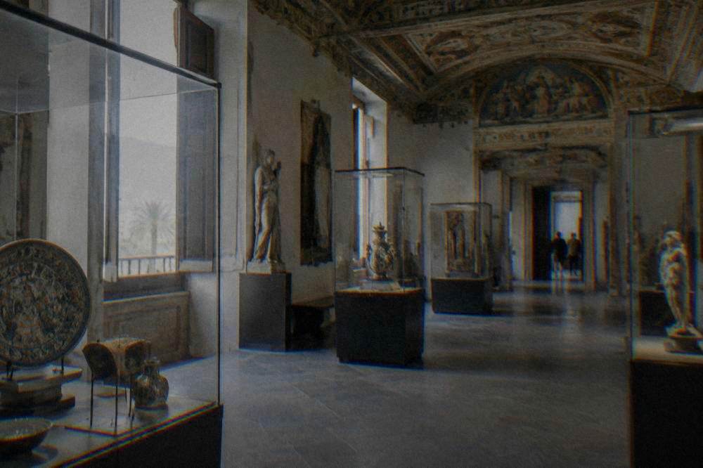 A museum gallery in Palermo with glass display cases and painted ceilings above stone floors