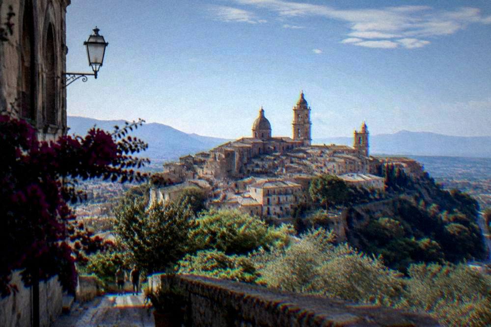 A hilltop Sicilian town of stone houses and bell towers seen across a valley
