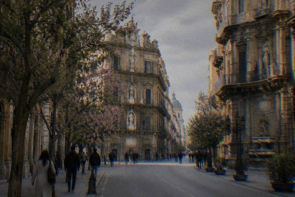 A tree-lined Palermo avenue in spring with warm light on ornate buildings and people walking