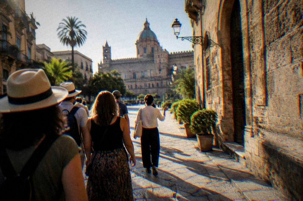 A group of visitors following a tour guide along a sunlit stone street in old Palermo
