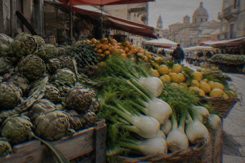Baskets of artichokes, fennel and citrus fruit lined up at a Palermo market stand