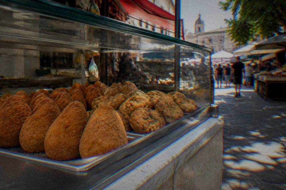 Fried arancine and chickpea fritters arranged behind the glass of a Palermo street food counter
