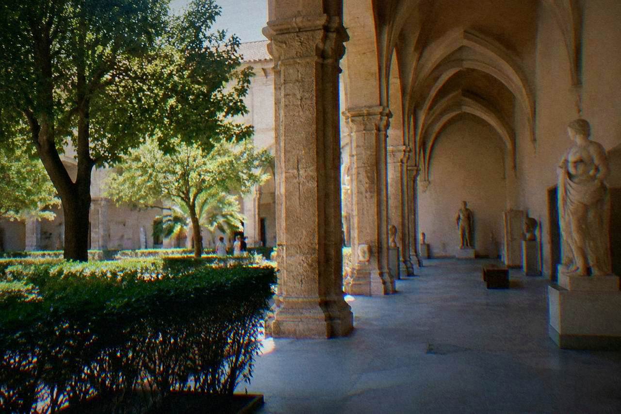 A museum gallery in Palermo with stone arches and sculpture displays lit by warm daylight