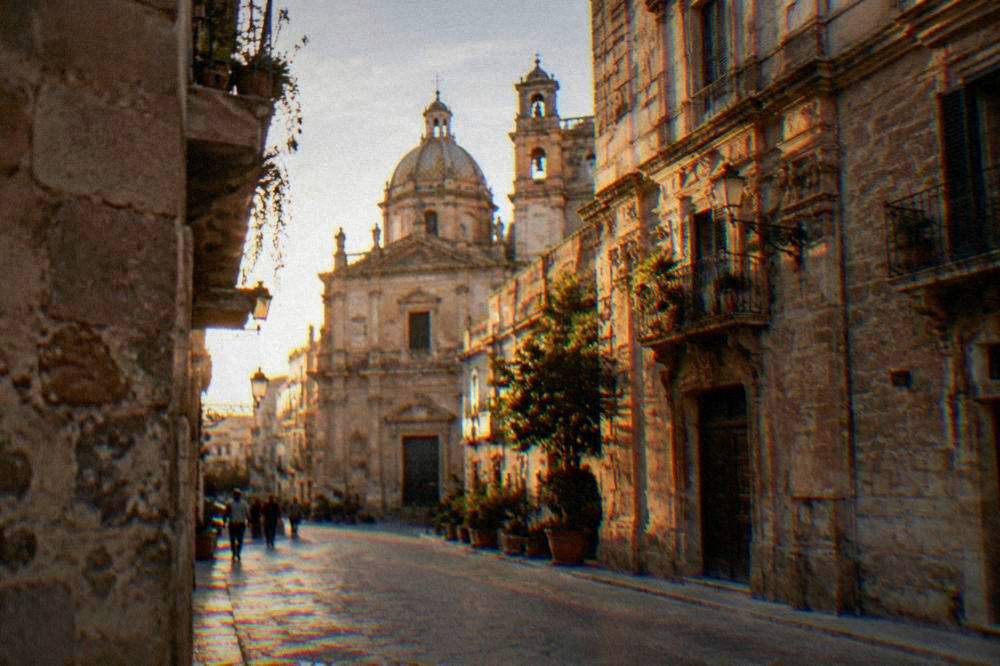 A historic Palermo street with worn stone buildings and a church facade in daylight