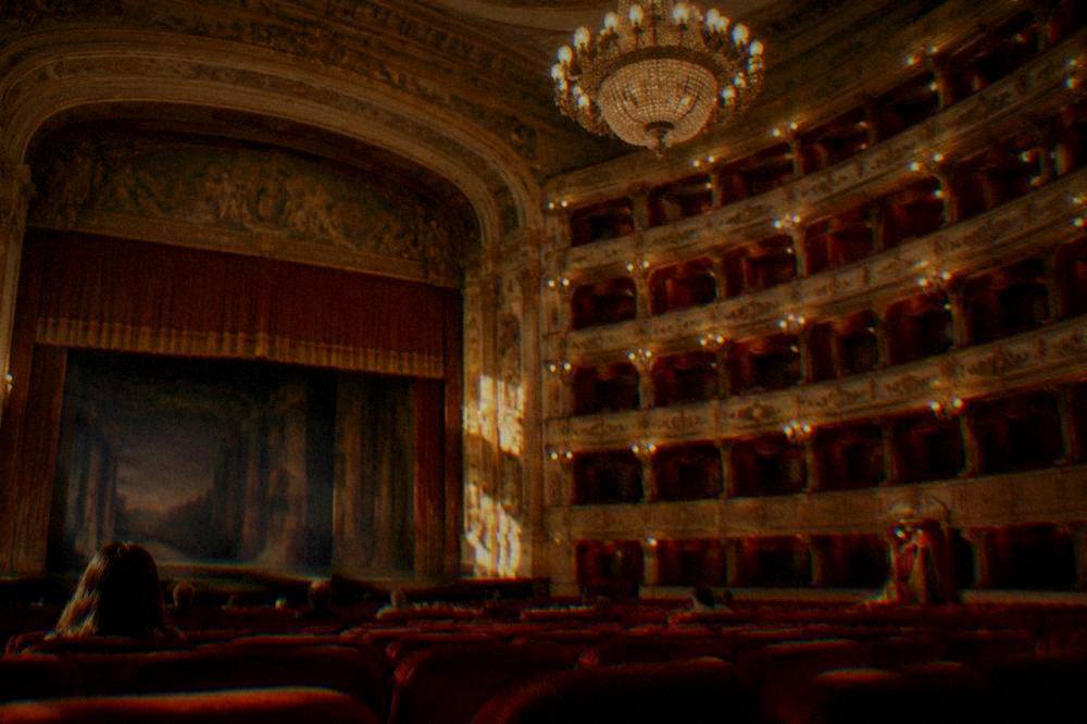 The grand auditorium of an opera house with red seating, boxes and a chandelier