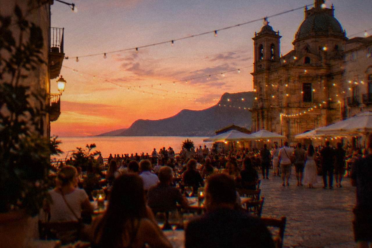 Evening crowd in a Palermo square with string lights above outdoor tables