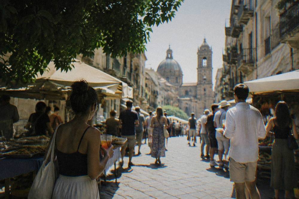 People standing with drinks and paper food trays in a narrow lit market street
