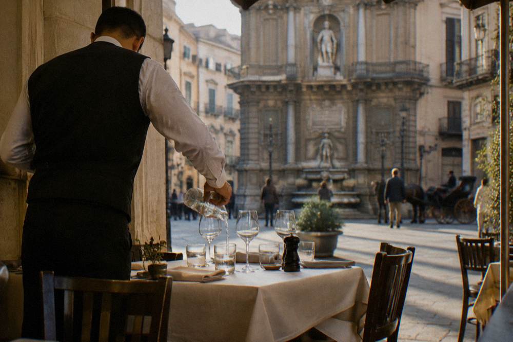 Waiter pouring water into glasses at a set restaurant table in a Palermo dining room