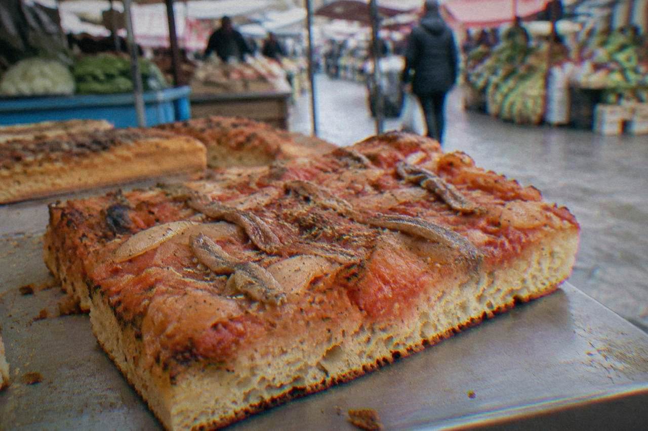 A thick slice of sfincione pizza topped with onion and anchovy on a market counter in Palermo