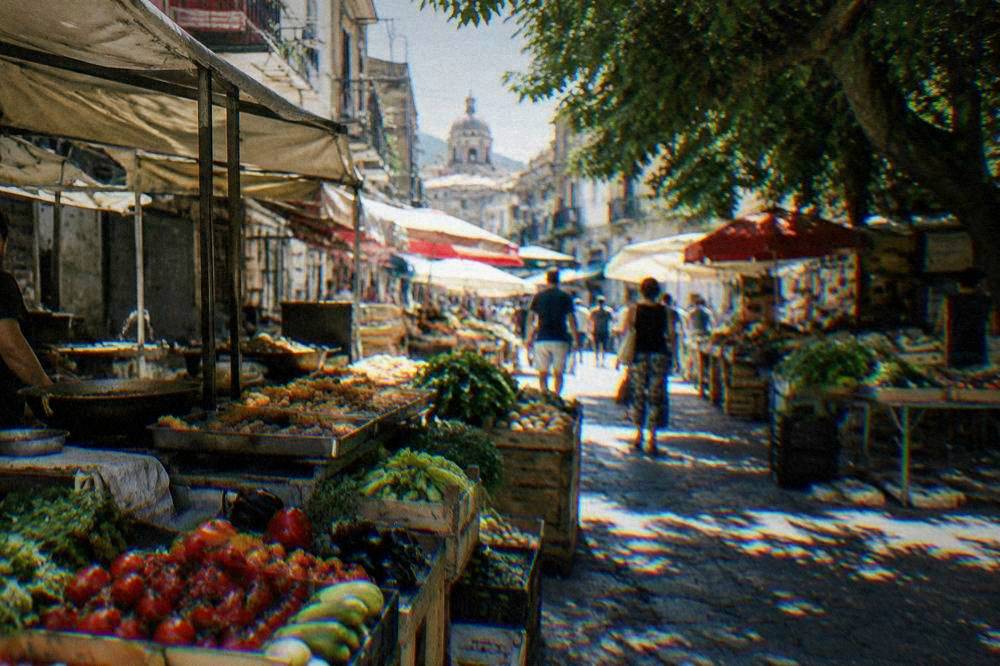 A busy BallarÃ² market lane in Palermo with stalls of vegetables and fried food in the morning