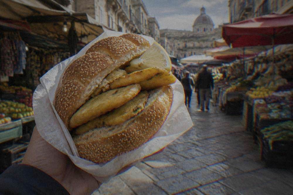 A sesame mafalda roll filled with hot panelle fritters and lemon, held in paper