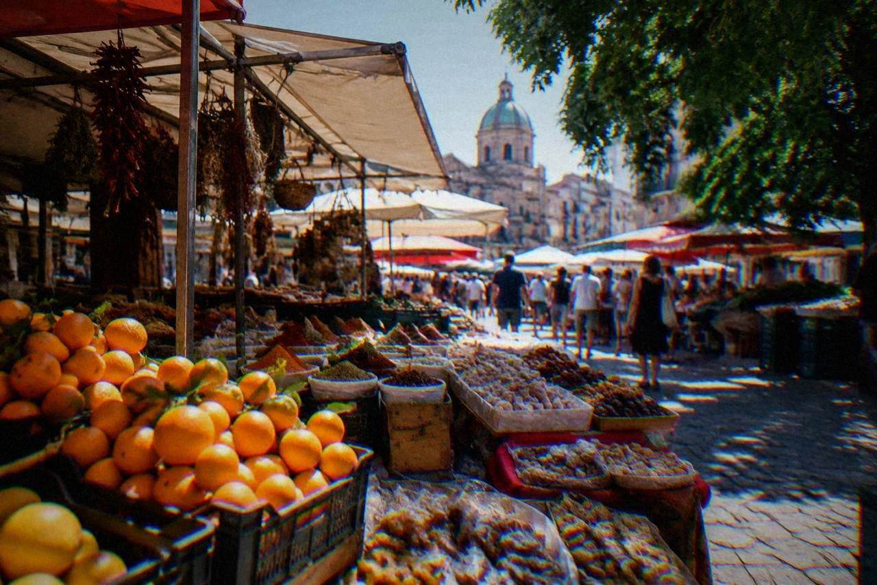 A busy Palermo street market stall with crates of oranges, spices and sweets under awnings