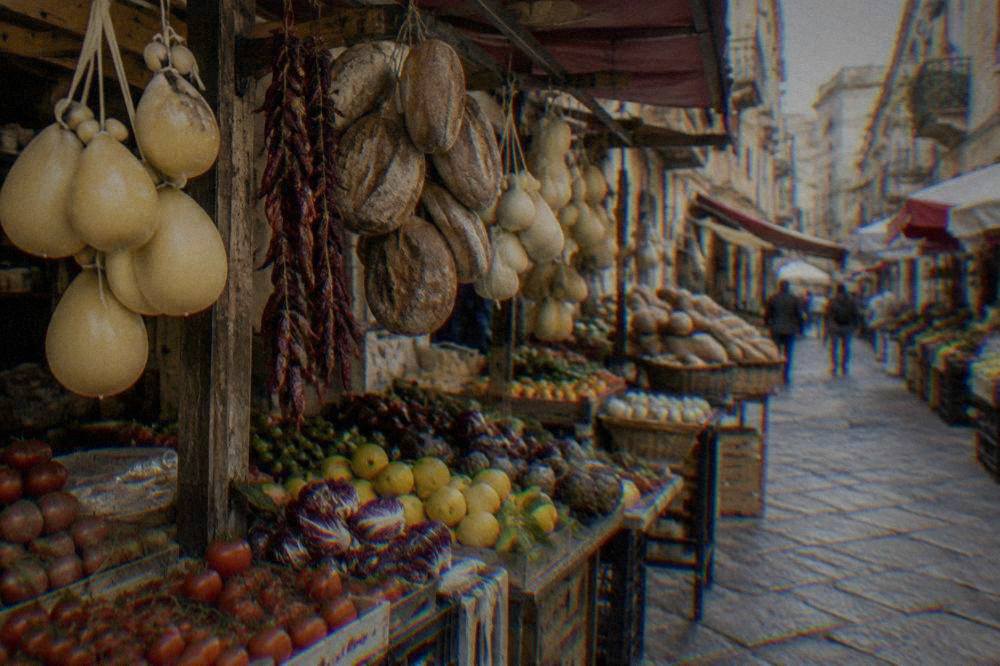 A produce stall in an old Palermo market alley with hanging cheese and bread