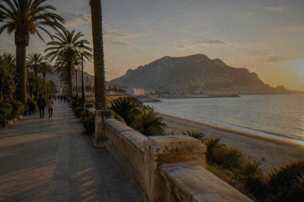 Palm-lined seafront promenade at Mondello with white sand and distant mountains