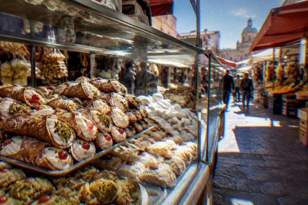 A shop counter displaying Sicilian cannoli and almond sweets under glass