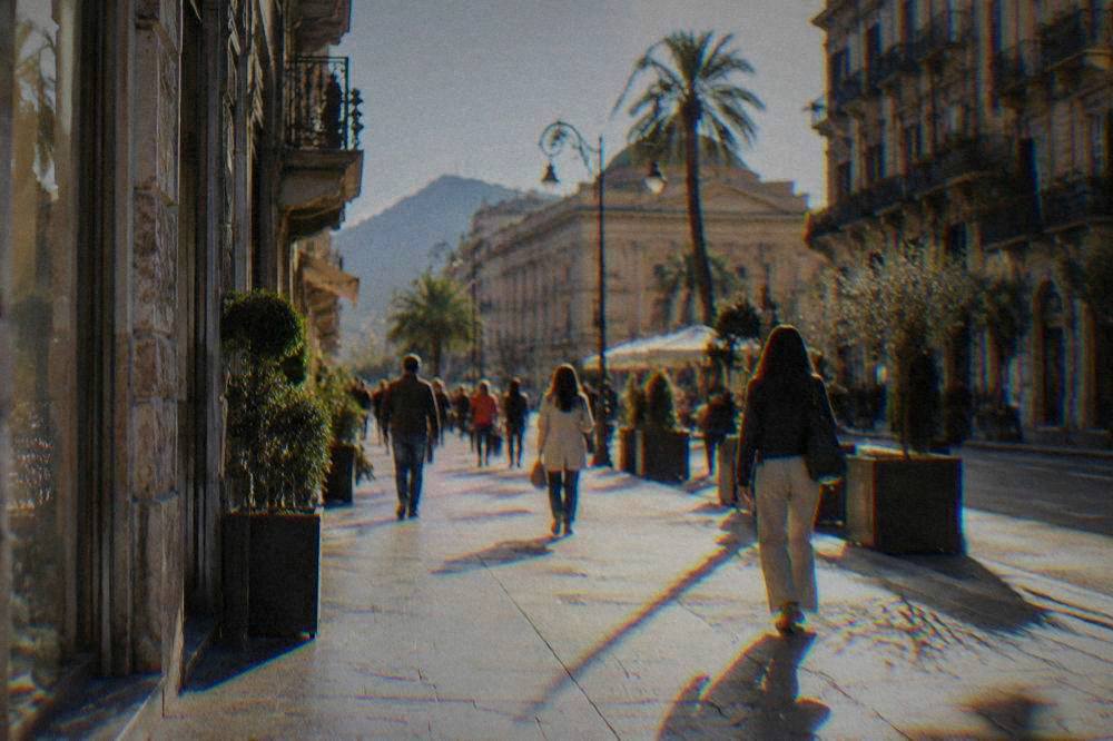 Shoppers walking along a sunlit Palermo shopping street with balconied buildings
