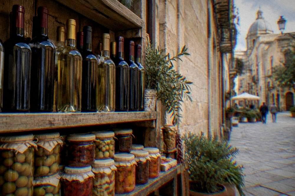 Bottles of Sicilian wine and jars of preserves arranged on a wooden shop shelf