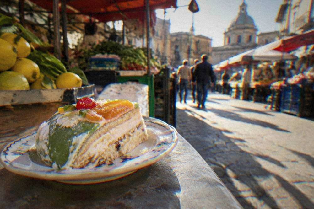 A slice of cassata cake with green marzipan, white icing and candied fruit on a small plate
