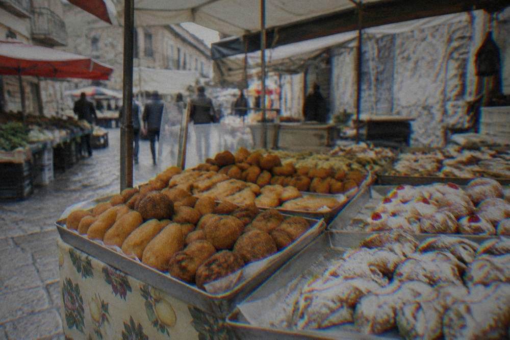 A market stall in Palermo with trays of fried snacks and sweets under a canvas awning