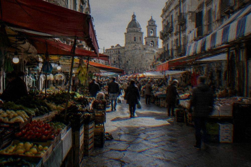 A narrow Palermo market street with awnings, produce stalls and shoppers