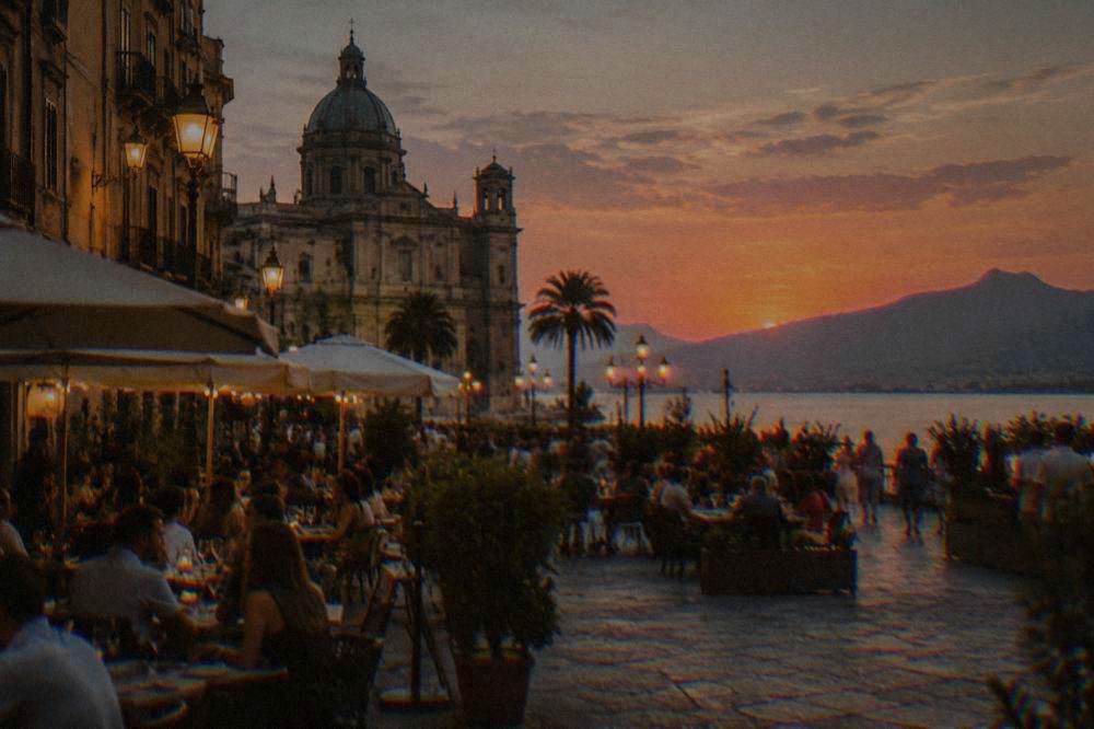 Crowds eating and drinking outdoors in a lit Palermo square in the evening