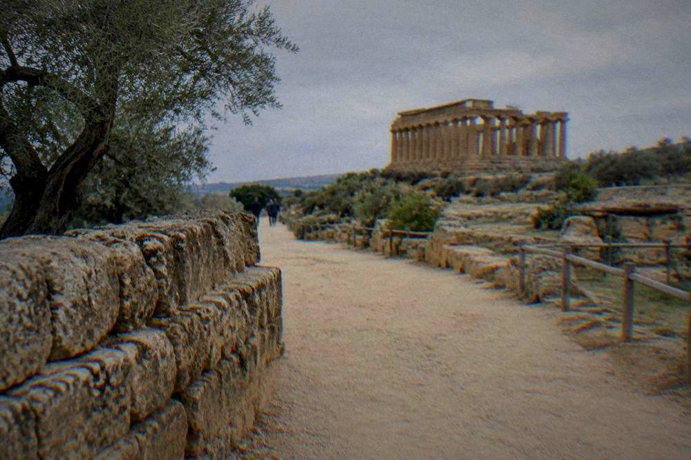 A wide walking path lined with ancient stone walls leading toward temple ruins