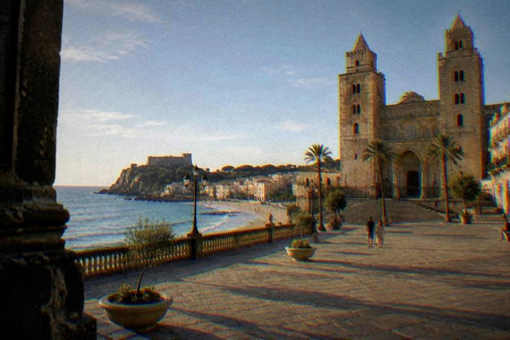A seaside town with a sandy beach below a rocky promontory and a twin-towered cathedral