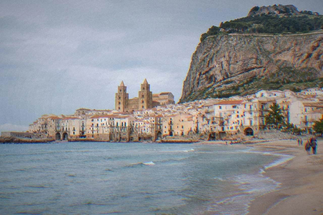Cefalu seen from the sea with the rocky headland of La Rocca above the town and the beach in the foreground