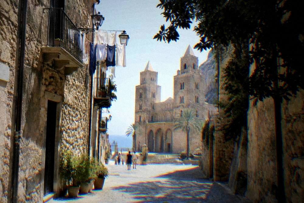 Narrow medieval street in Cefalu old town with stone buildings and laundry overhead