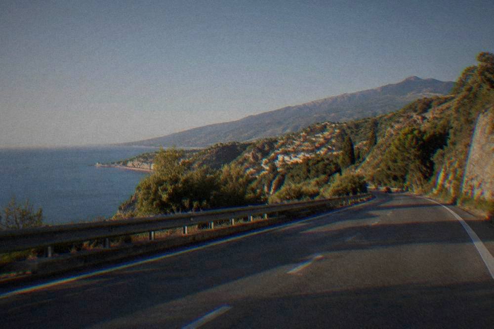 An empty motorway cutting through green Sicilian hills under a clear sky