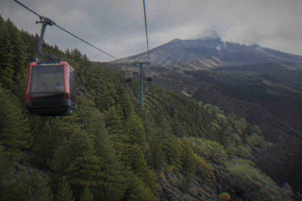 A cable car cabin ascending a forested volcano slope with dark lava rock nearby