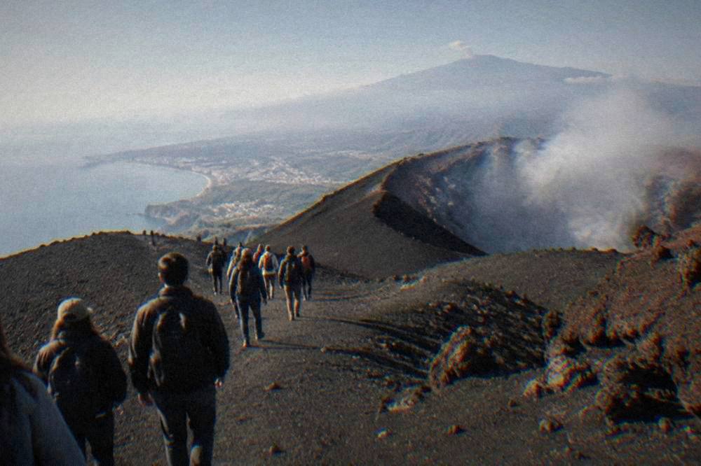 A tour group walking on dark volcanic ash paths near a smoking crater rim