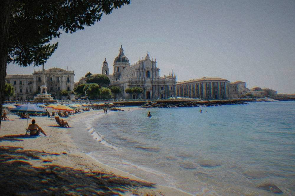 Sandy beach with clear shallow water and a line of coloured beach umbrellas